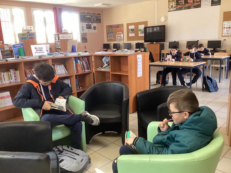 Collégiens assis dans des fauteuils, en train de lire un livre